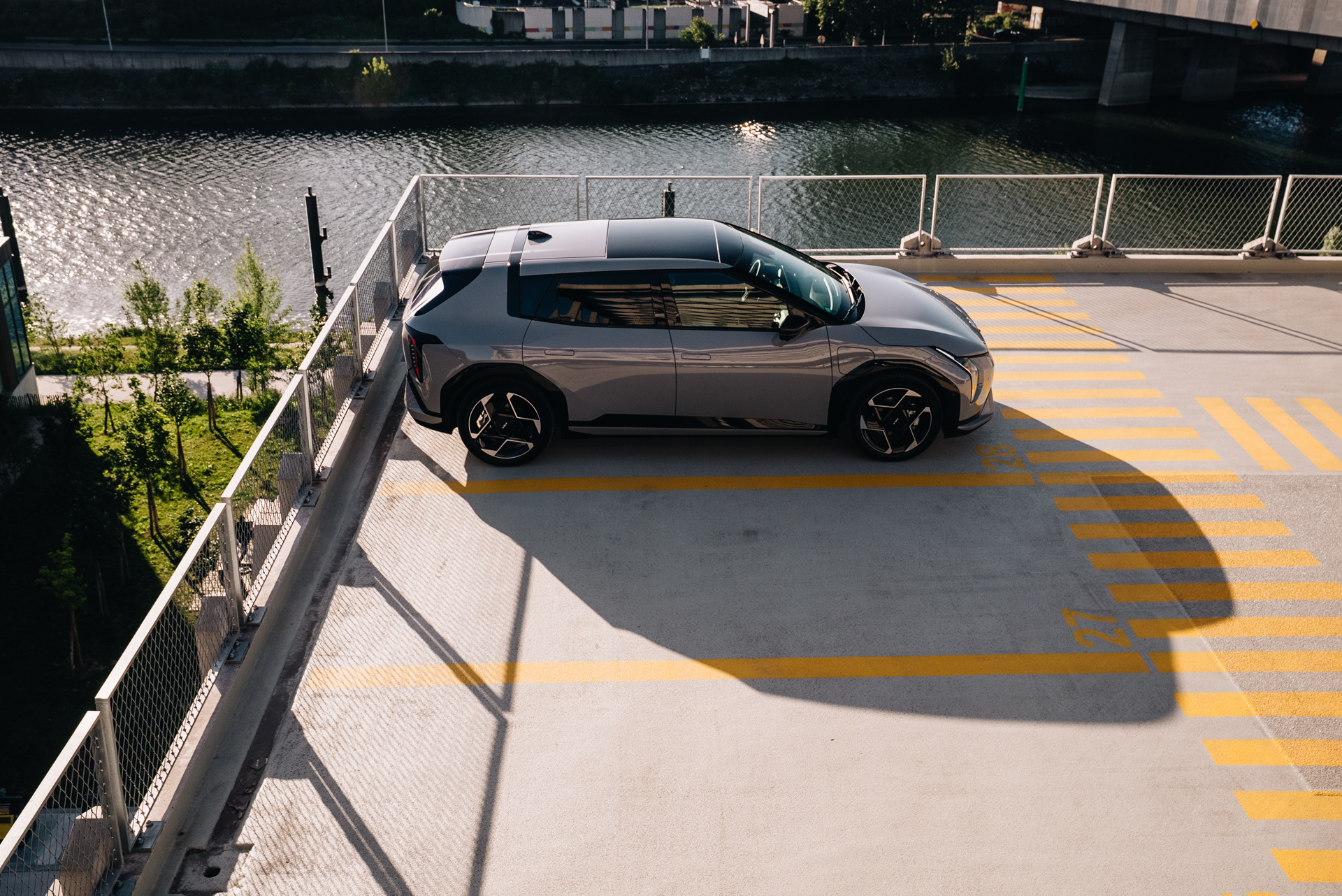 Kia EV4 grise vue de dessus, gar&eacute;e sur un parking en hauteur pr&egrave;s d'une rivi&egrave;re.