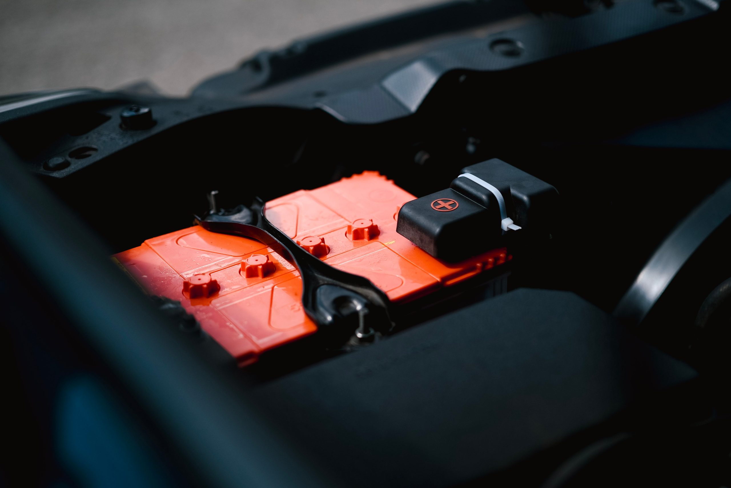 Batterie 12V orange install&eacute;e dans le compartiment moteur d'une voiture