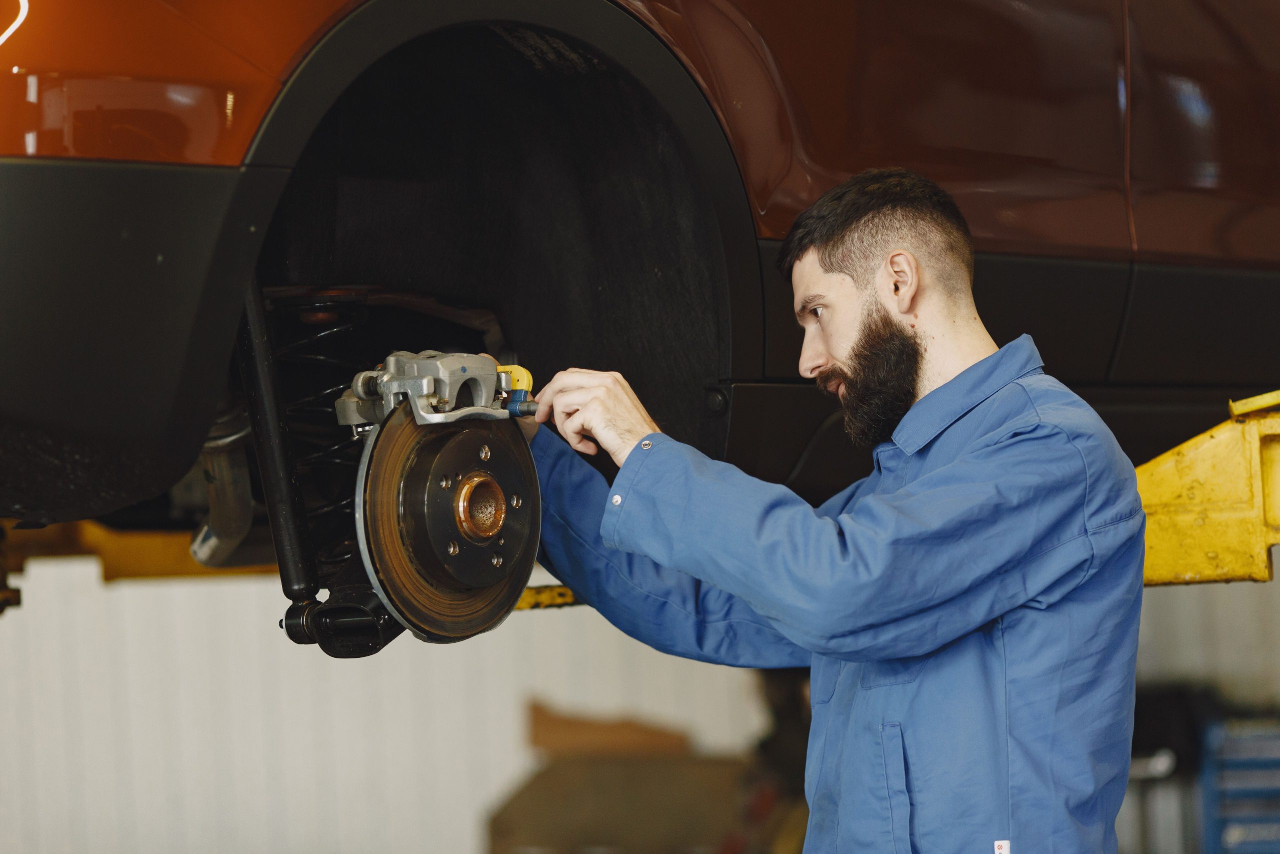M&eacute;canicien en uniforme bleu r&eacute;parant le syst&egrave;me de freinage d'une voiture en atelier